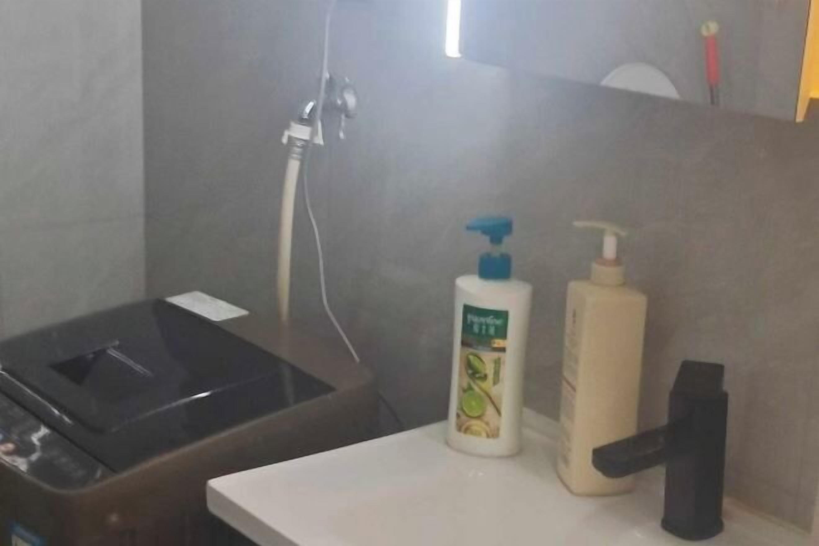 A bathroom with a shower, a trash bin, and two bottles of liquid soap.