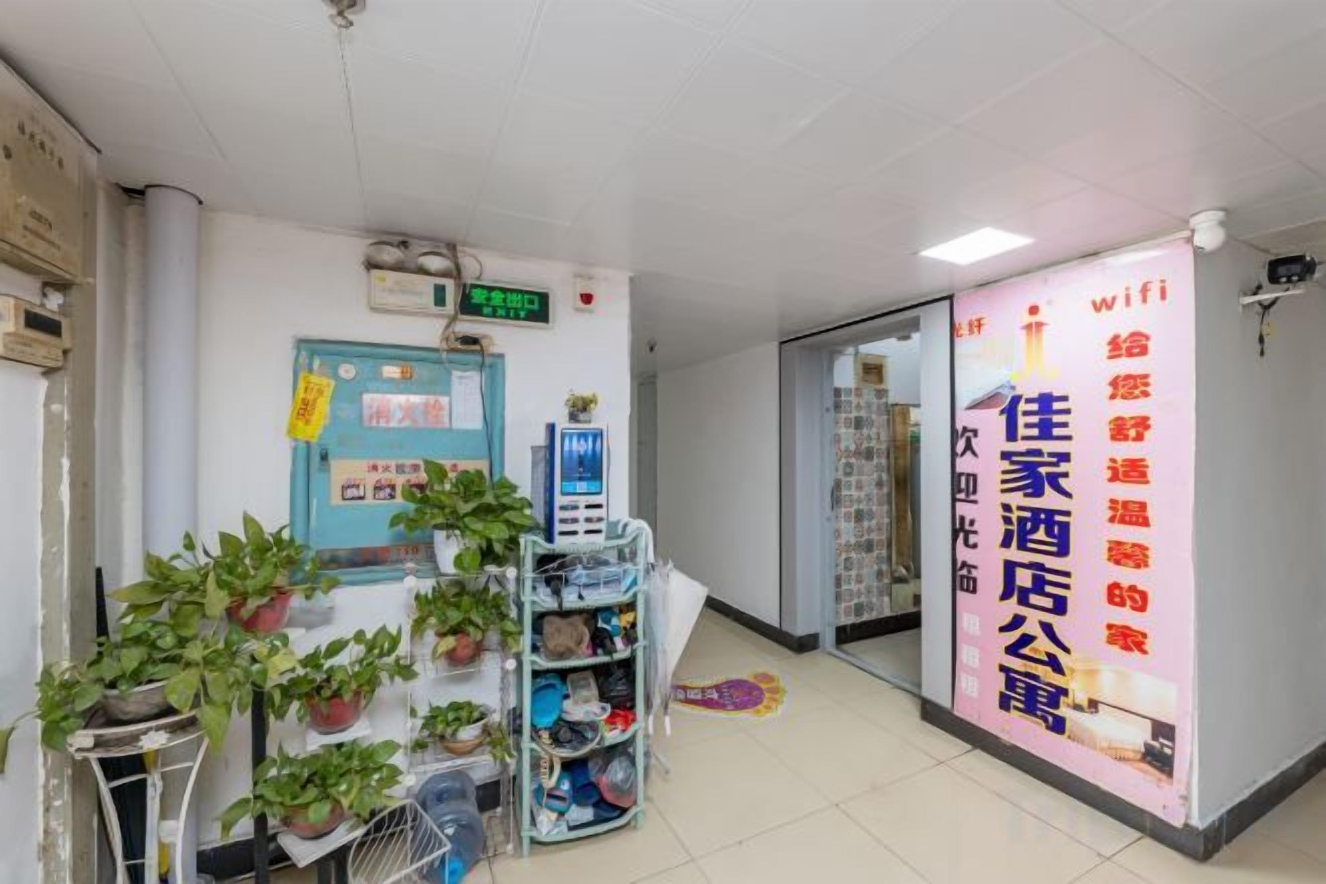 A hotel lobby with a reception desk, potted plants, a digital display, and a large promotional poster.