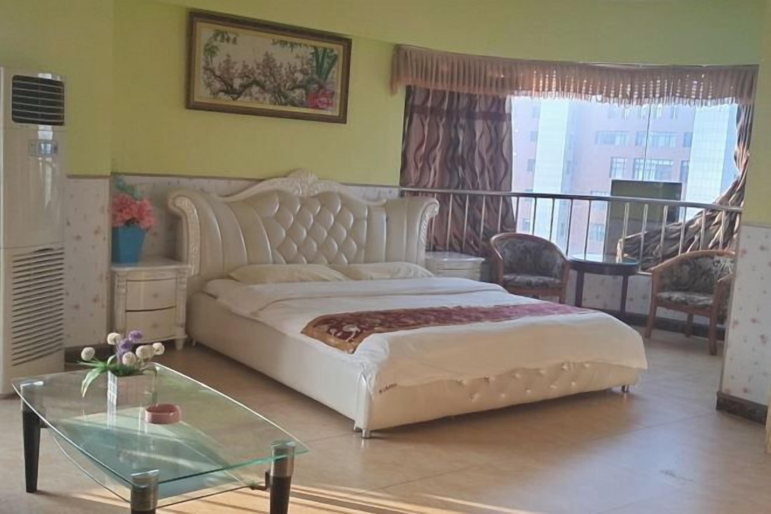 Un dormitorio con una cama, una mesita de vidrio, una silla, un escritorio y una ventana con cortinas.