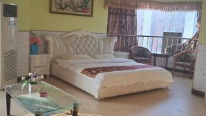 A bedroom with a bed, a glass coffee table, a chair, a desk, and a window with curtains.