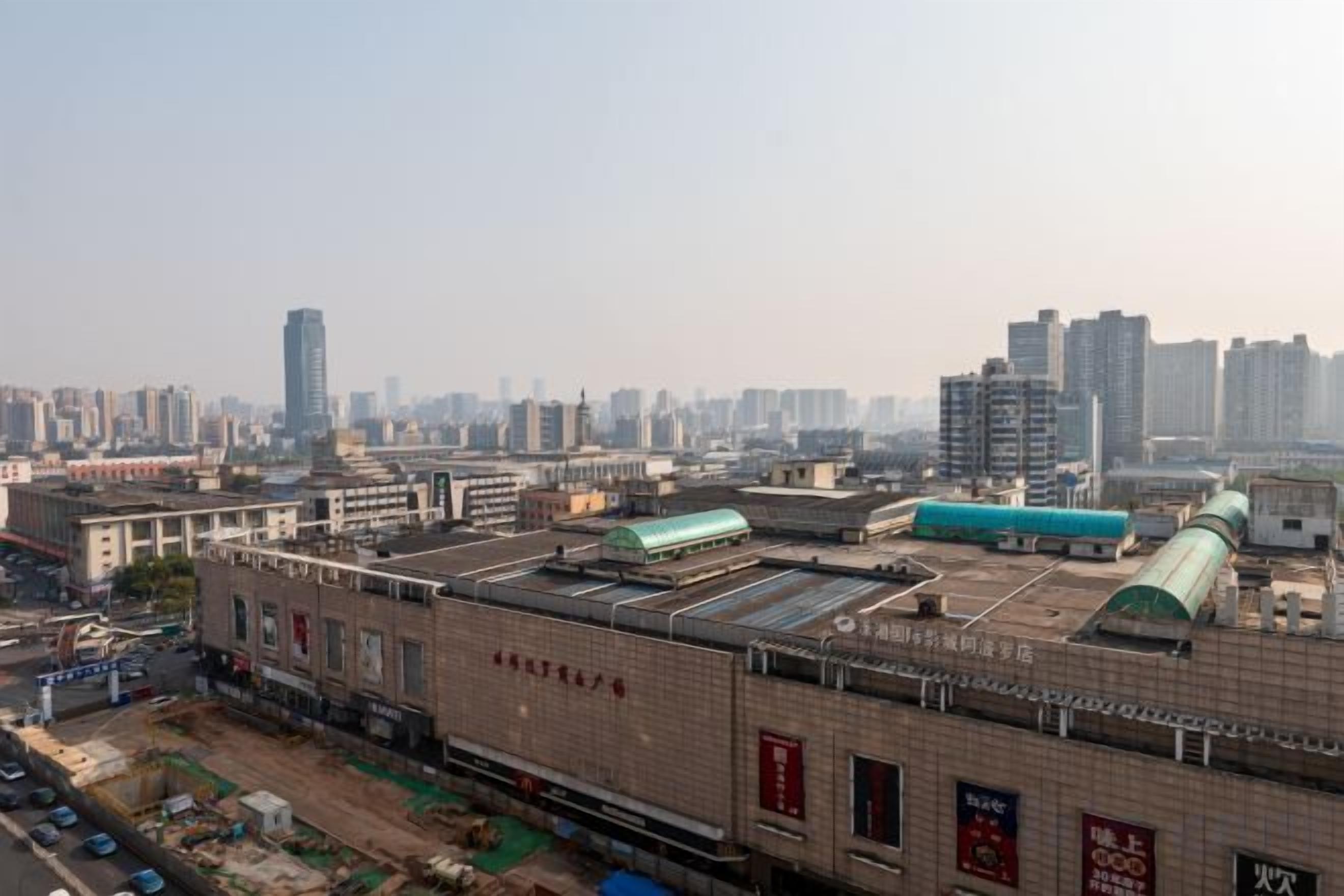 A large industrial building with multiple levels and a flat roof, surrounded by a cityscape with high-rise buildings.