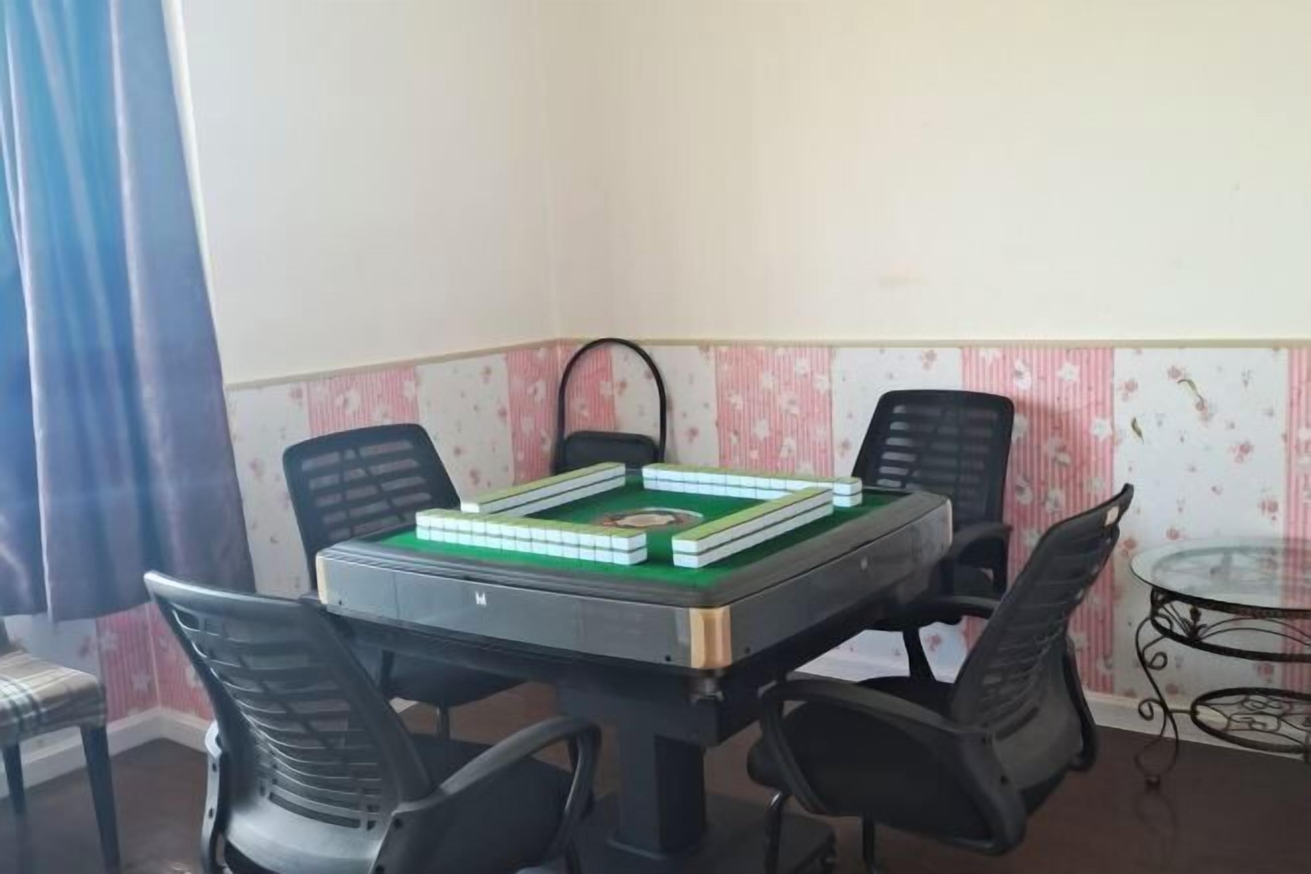 Una habitación con una mesa dispuesta para un juego, cuatro sillas, una pequeña mesa de cristal y papel tapiz estampado.