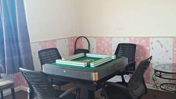 Una habitación con una mesa dispuesta para un juego, cuatro sillas, una pequeña mesa de cristal y papel tapiz estampado.