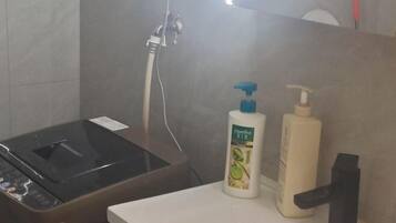 Un baño con lavamanos, cabezal de ducha de mano y dos botellas de jabón líquido.