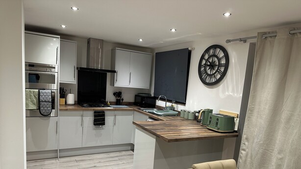 A modern kitchen with white cabinets, a wooden countertop, and a dining area with a table and chairs.