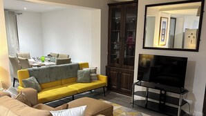 A living room with a beige sofa, yellow sofa, and a TV on a stand.