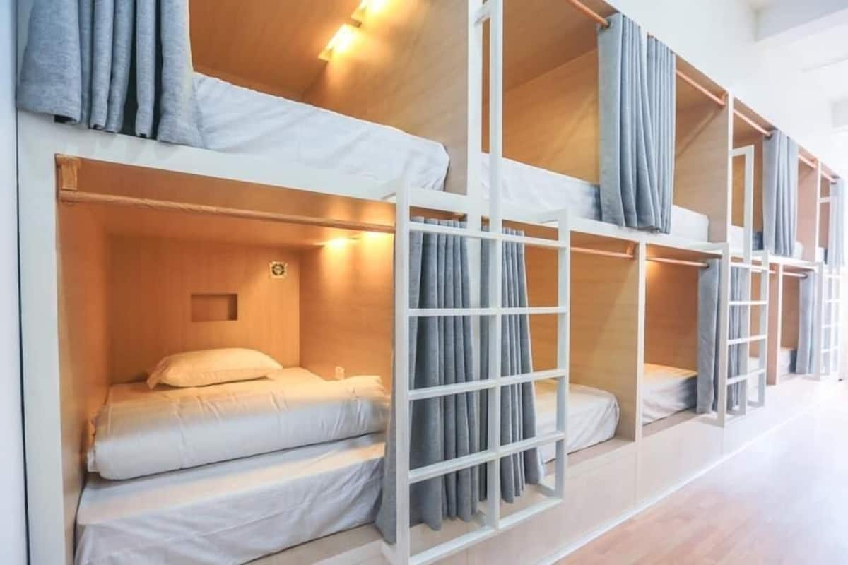 Une chambre avec un lit superposé, dotée de linge de lit blanc et de rideaux gris.