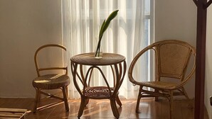 Una habitación con dos sillones de mimbre, una mesita redonda con un florero y un perchero de madera.