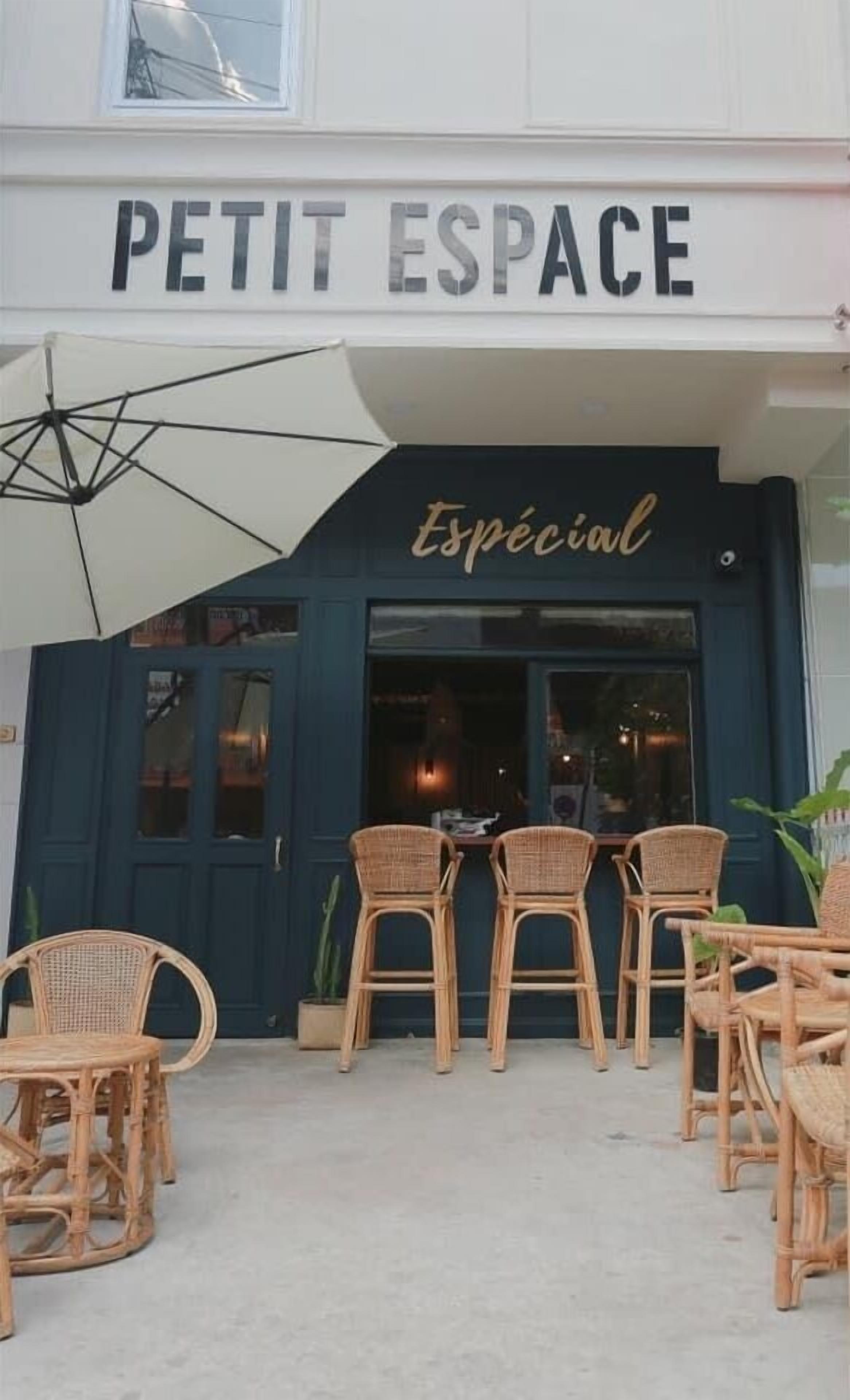 A building with a sign reading "PETIT ESPACE" and "Espécial" below it. There are wicker chairs and a table outside the entrance.