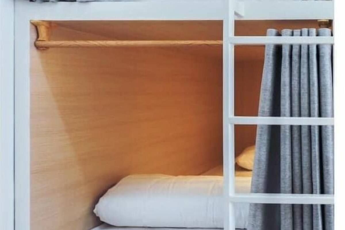 Un lit superposé avec une échelle, du linge de lit blanc et des rideaux gris.
