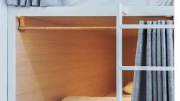 Una cama litera con escalera, ropa de cama blanca y cortinas grises.