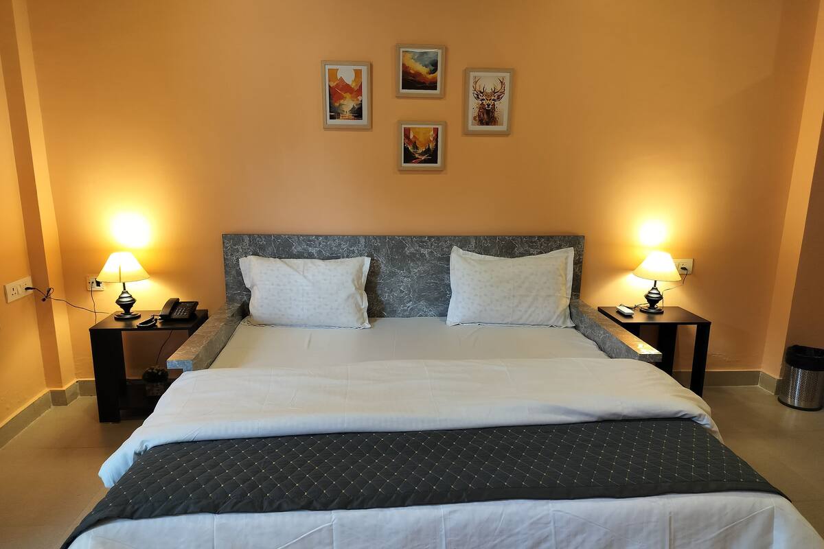 Une chambre d’hôtel avec un grand lit, deux tables de chevet avec des lampes, une tête de lit en marbre et trois tableaux encadrés accrochés au mur.