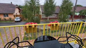 Varanda com duas cadeiras de metal preto e uma pequena mesa redonda, com vista para uma área residencial com casas e uma rua.