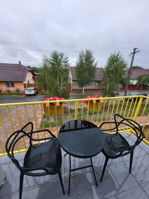 Un balcon avec deux chaises en métal noir et une petite table ronde, donnant sur un quartier résidentiel avec des maisons et une rue.