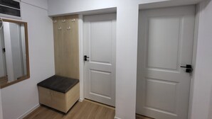 Um corredor com um banco de madeira, um espelho e três portas brancas.