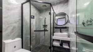 A modern bathroom with a glass-enclosed shower, a white toilet, a sink with a mirror, and a shelf with towels. - Yumei Yipin Hotel (Guangzhou Panyu Shiqiao Branch) (Guangzhou)