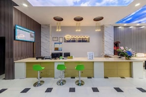A reception area with a desk, three green bar stools, a digital screen, and a wall-mounted sign. - Yumei Yipin Hotel (Guangzhou Panyu Shiqiao Branch) (Guangzhou)