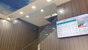 A hotel reception area with a wooden wall, a glass staircase, and a digital display board. - Yumei Yipin Hotel (Guangzhou Panyu Shiqiao Branch) (Guangzhou)