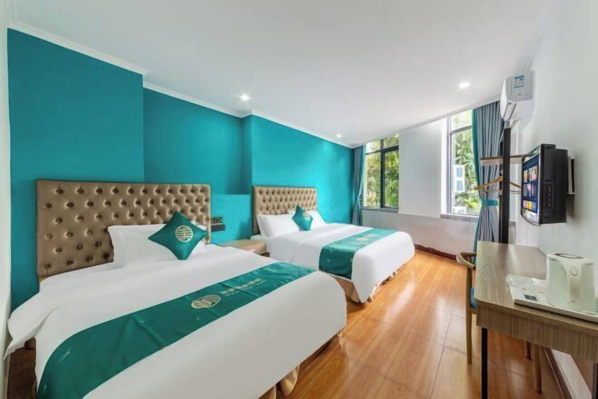 Une chambre d’hôtel avec deux lits, des murs de couleur turquoise, un plancher en bois, une télévision et un bureau avec une machine à café.