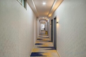 En lång, smal hotellkorridor med dörrar på båda sidor och ett mattbeklätt golv.