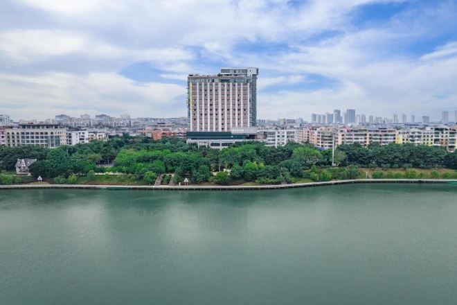 A high-rise building with a modern design, surrounded by a body of water and greenery.