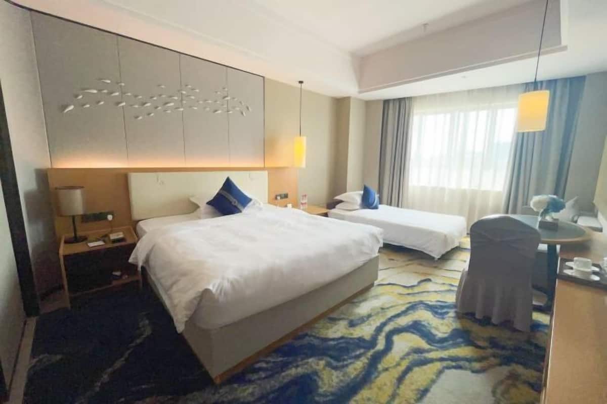Hotelkamer met een groot bed, een kleiner bed, een bureau, een stoel, een lamp en een decoratief wandpaneel.