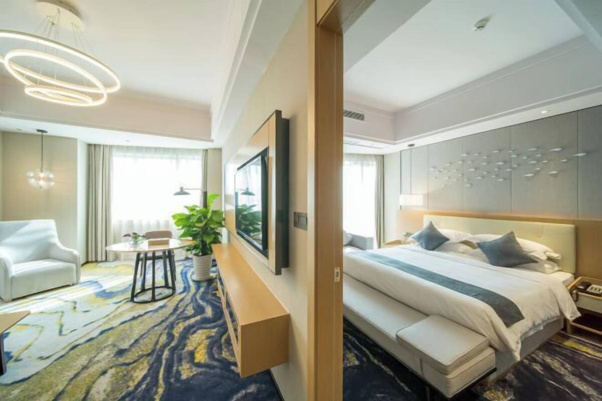 Een moderne hotelkamer met een groot bed, een zithoek met een bank en stoelen, een kleine tafel en een potplant.