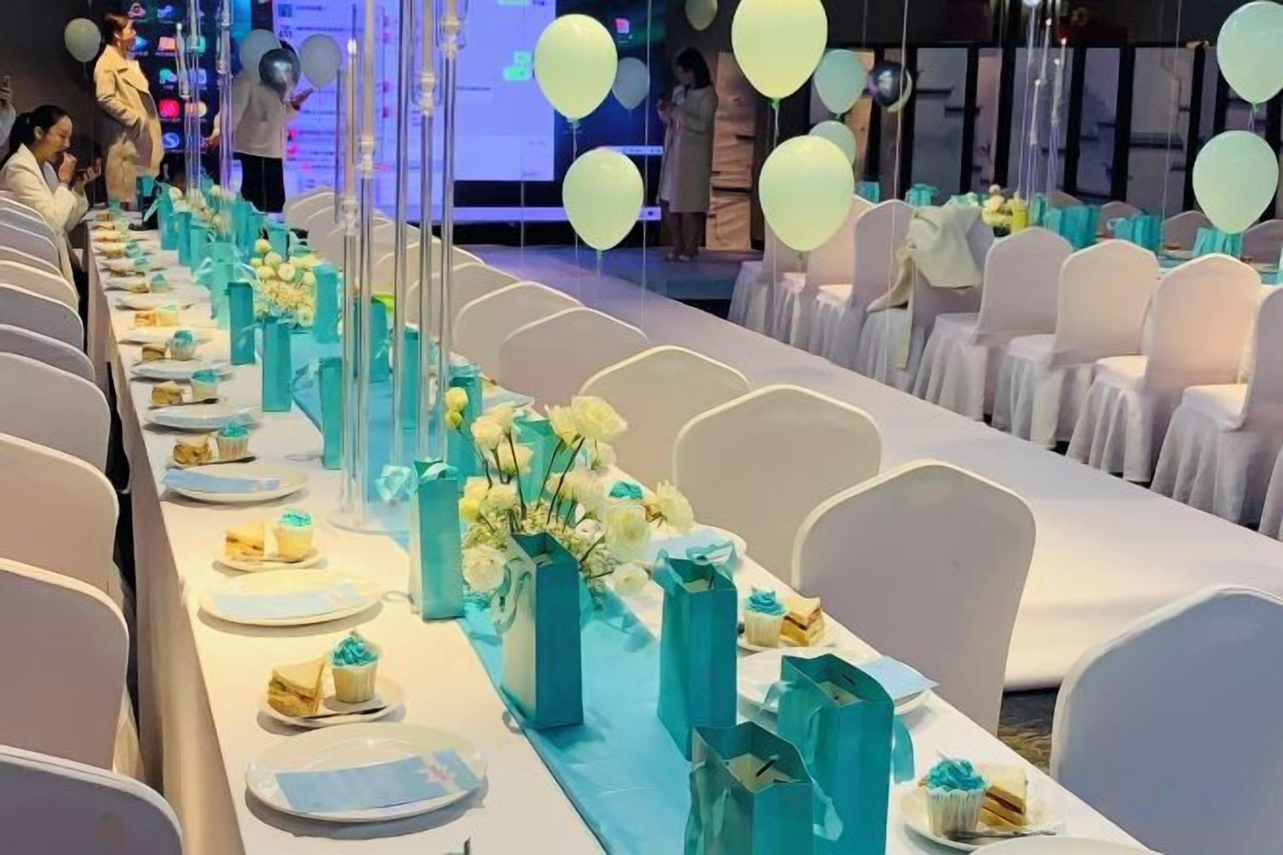 A banquet hall with long tables set for a formal event, featuring floral centerpieces and a row of chairs.