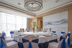 A banquet hall with round tables, chairs with blue sashes, a chandelier, and a large wall painting. - GanZhouXiangjiangwan International Hotel (South Gate Ancient City Wall) (Ganzhou)