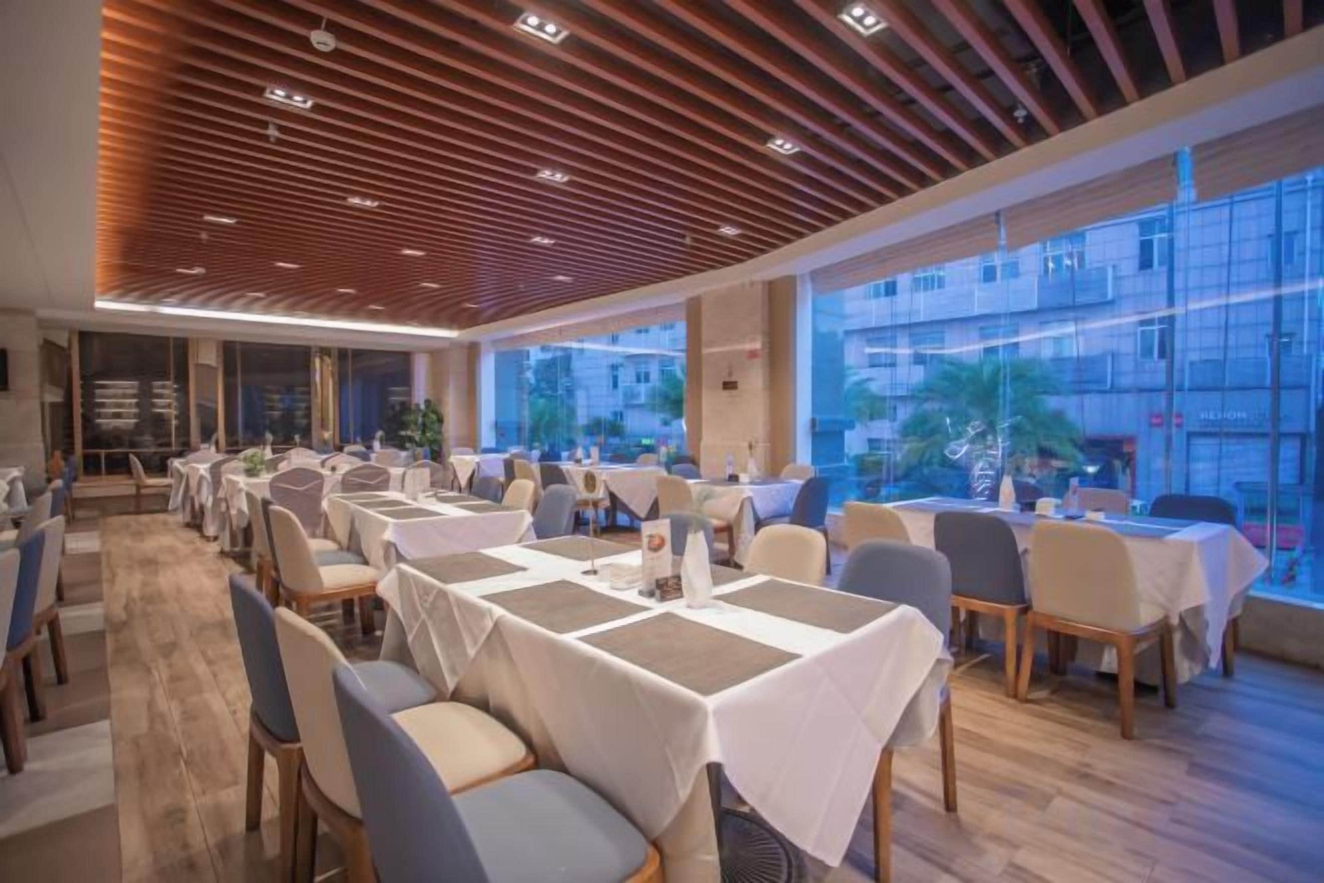 Un restaurante con mesas dispuestas para comer, ventanas amplias y un diseño de techo moderno.