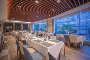 Un restaurante con mesas dispuestas para comer, ventanas amplias y un diseño de techo moderno.