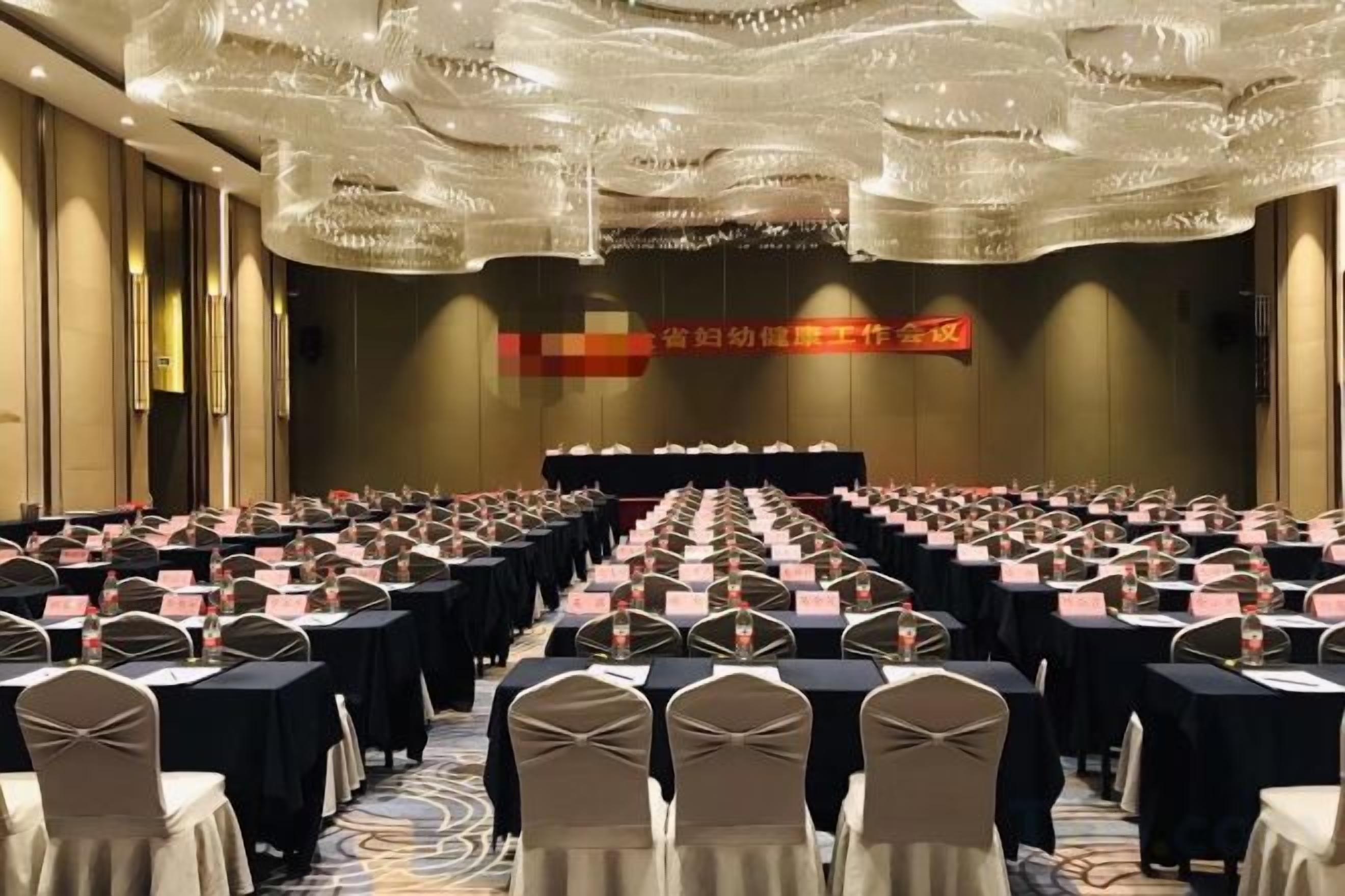 A conference room with rows of tables and chairs, a stage at the front, and a large banner on the wall.