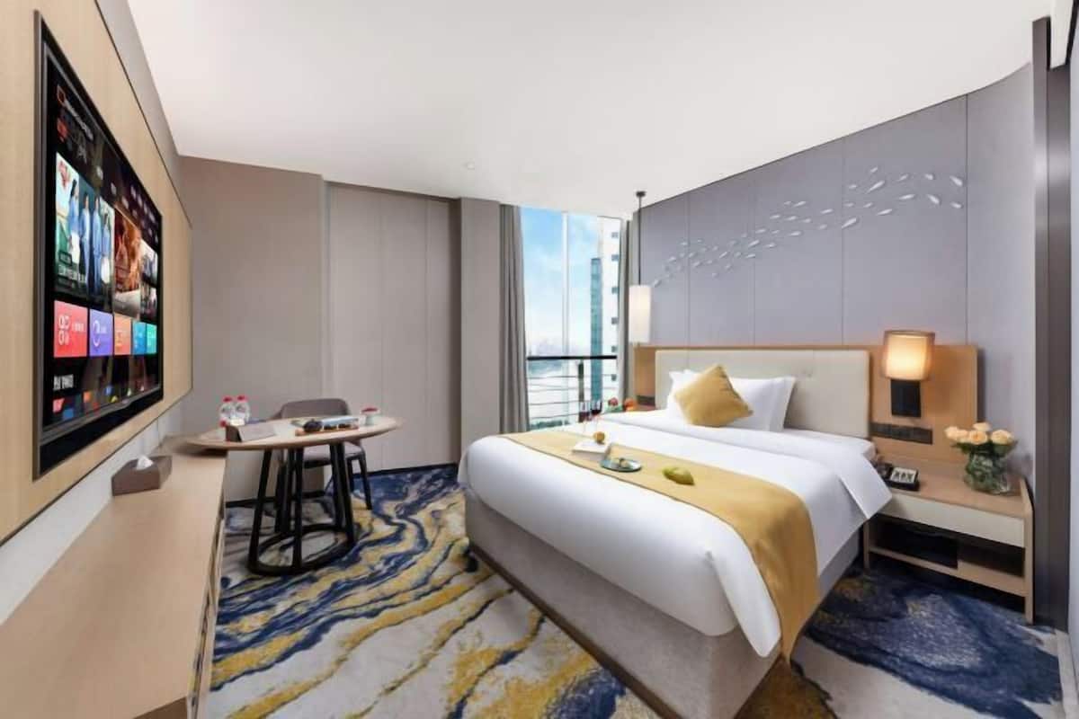 Een hotelkamer met een bed, een bureau, een stoel, een aan de muur bevestigde televisie en een raam.