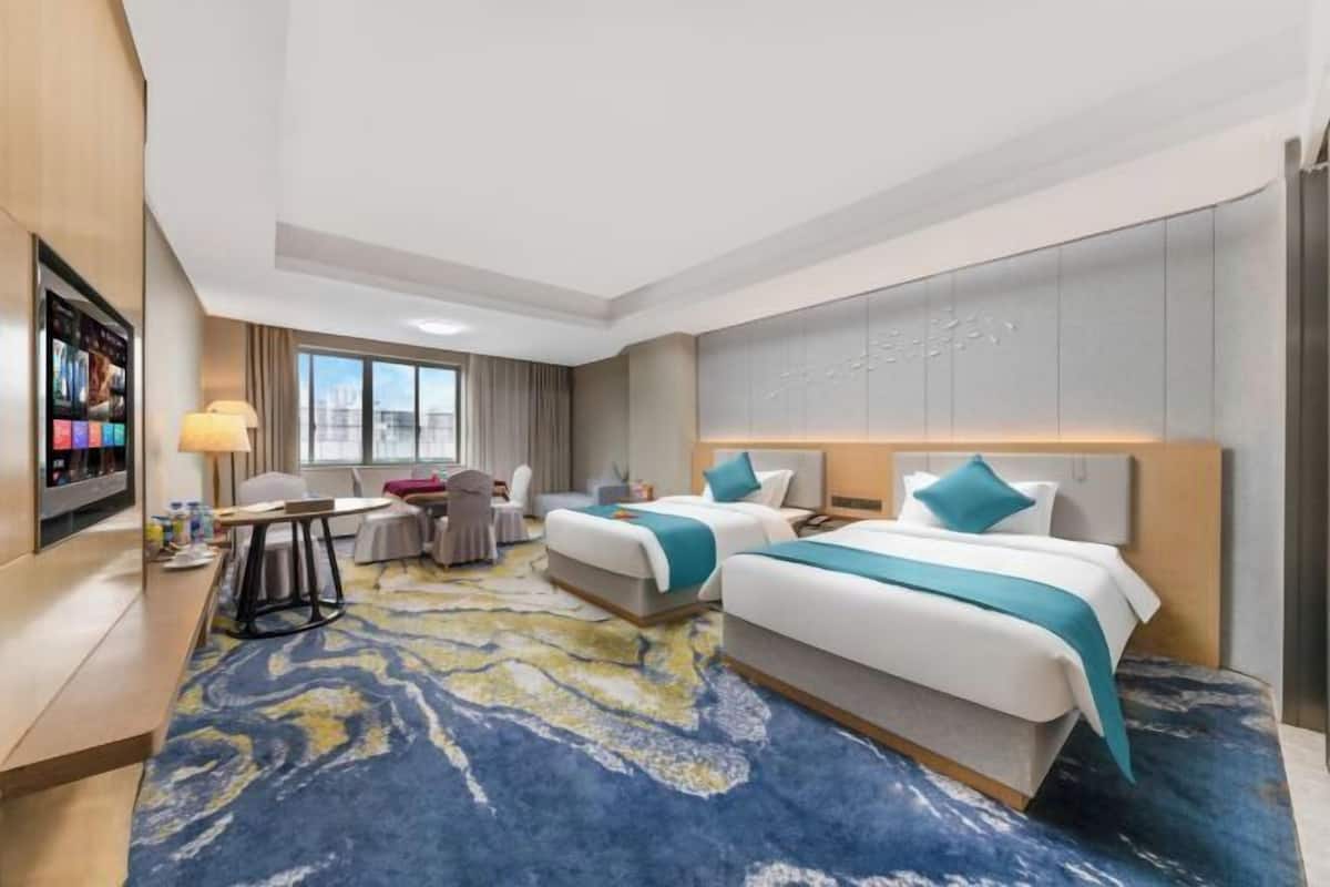 Een hotelkamer met twee bedden, een bureau, een stoel, een televisie en een groot raam.