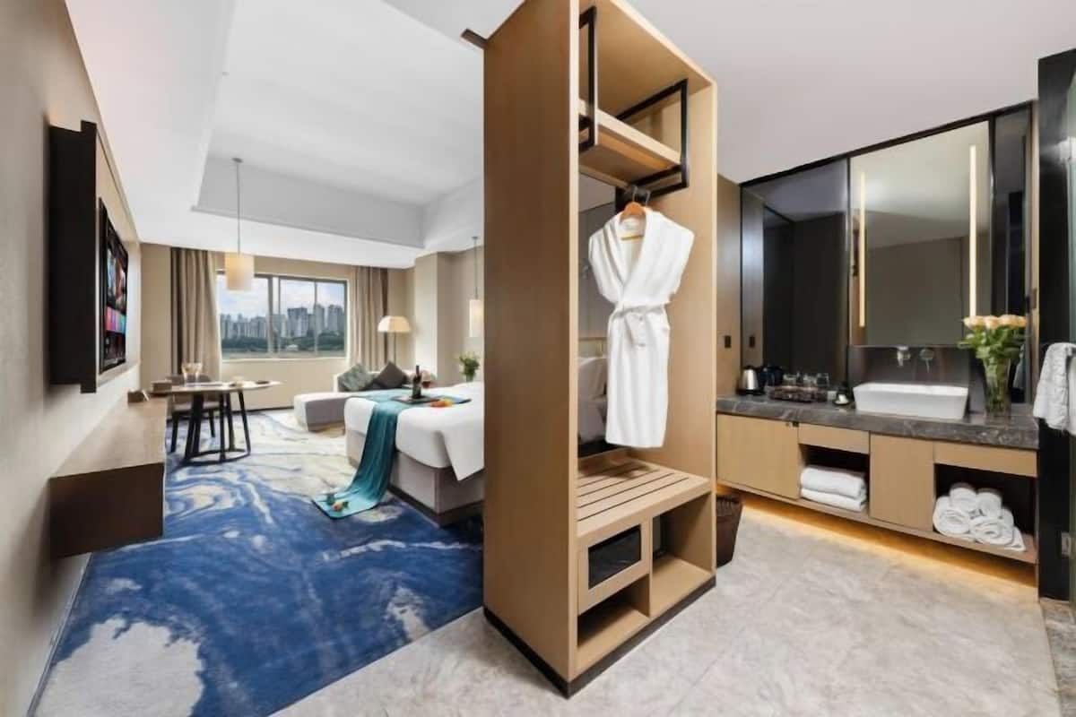 Een moderne hotelkamer met een bed, een zithoek, een kaptafel met spiegel en uitzicht op de stad.