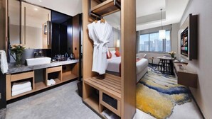 A modern hotel room with a large mirror, a built-in vanity, a robe hanging, a bed with a city view, and a small table with a vase. - GanZhouXiangjiangwan International Hotel (South Gate Ancient City Wall) (Ganzhou)