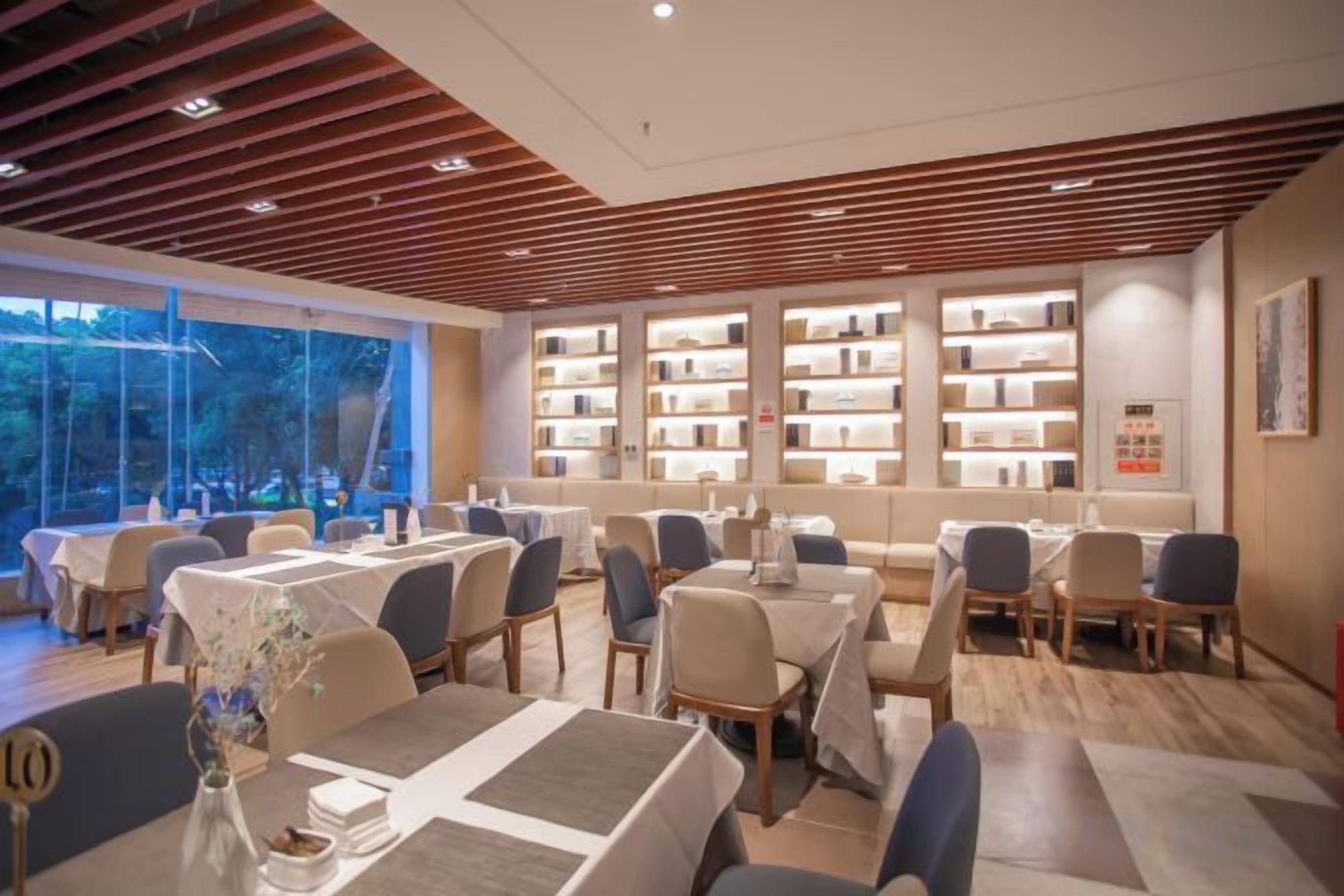 A restaurant with multiple tables and chairs, a wooden ceiling, and bookshelves in the background.
