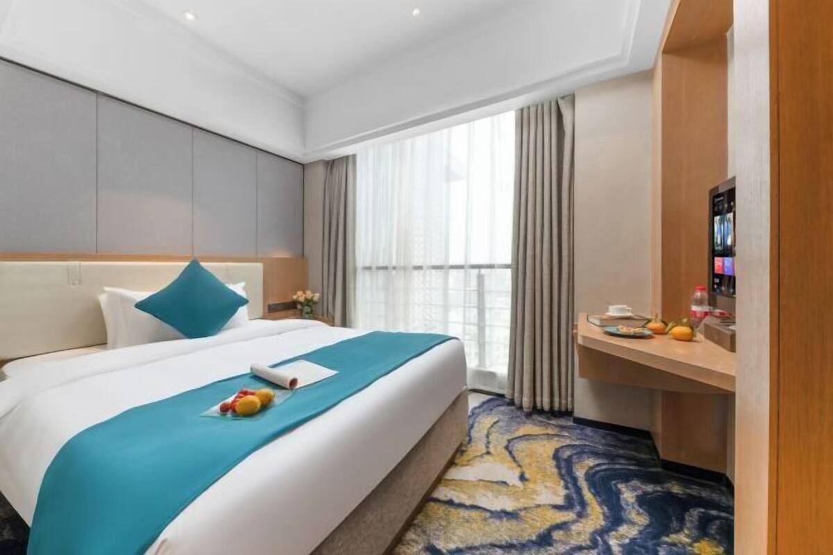 Een hotelkamer met een bed, een bureau, een televisie en een raam met gordijnen.