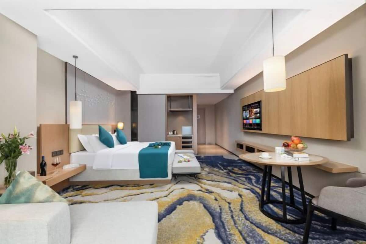 Een moderne hotelkamer met een bed, nachtkastje, lamp en een kleine ronde tafel met een fruitschaal.