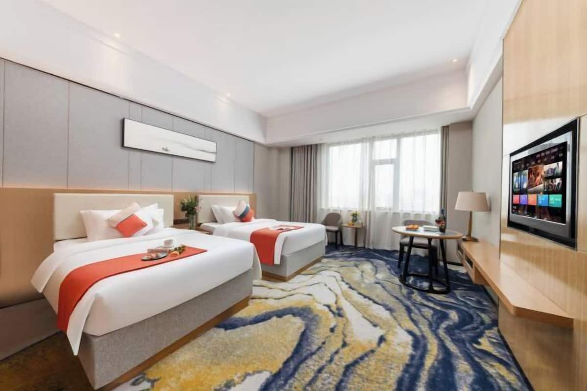 Een hotelkamer met twee bedden, een televisie, een klein tafeltje en een groot raam.
