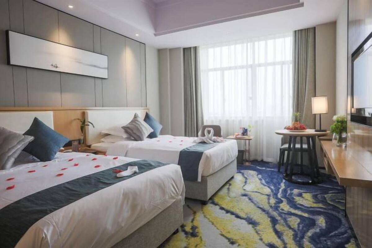 Een hotelkamer met twee bedden, een bureau, een stoel, een televisie en een raam met gordijnen.