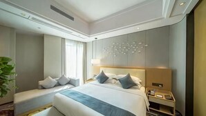 Une chambre d’hôtel avec un grand lit, une table de chevet, une commode, une lampe et une plante.