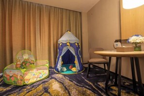 Een hotelkamer met een speeltent, een groene stoel, een tafel met een bloevas en een stoel.