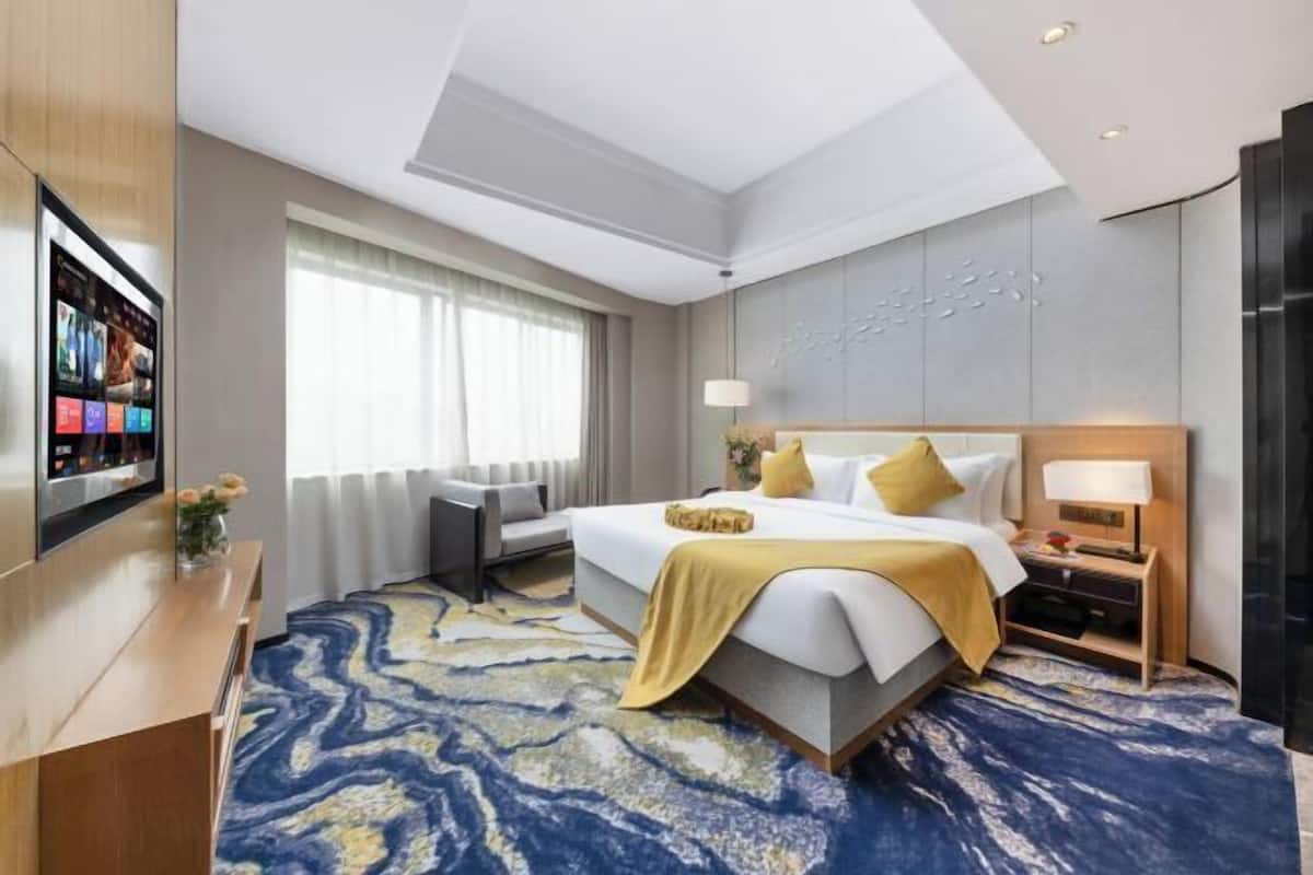 Een hotelkamer met een bed, nachtkastjes, een televisie, een bureau en een groot raam.