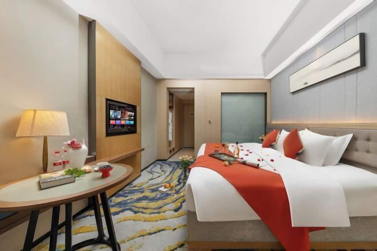 Een hotelkamer met een bed, een klein tafeltje met een lamp, een televisie en een deur die naar een andere kamer leidt.