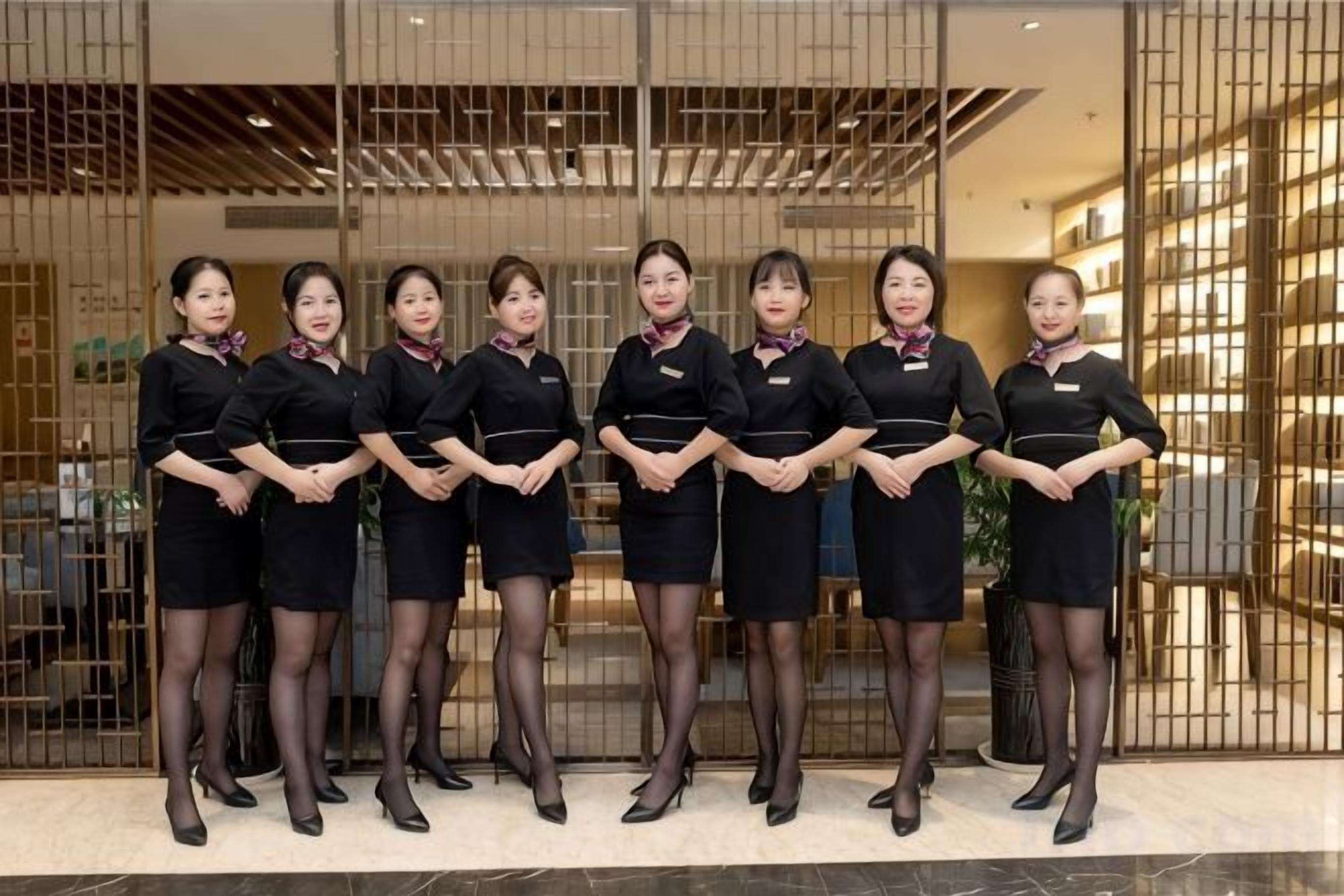 A group of uniformed staff members standing in front of a reception area with a modern interior design, including a reception desk and a seating area.