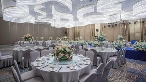 Une salle de banquet avec des tables rondes dressées pour le repas, chacune agrémentée d’un centre de table et entourée de chaises.