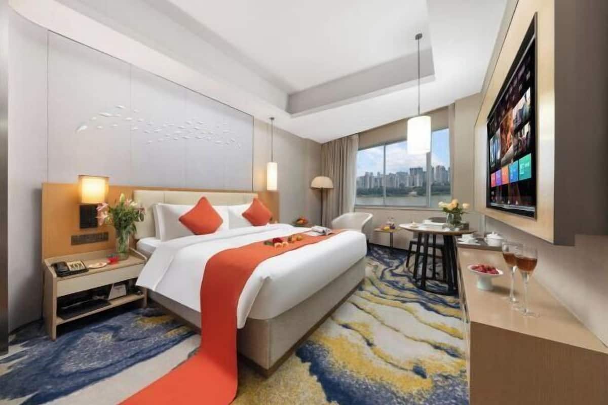 Hotelkamer met een bed, nachtkastje, lamp, stadszicht en een bureau met stoel.