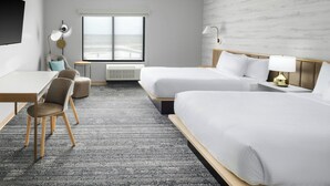 Habitación de hotel con dos camas, un escritorio, una silla, una mesita y ventana con vistas.