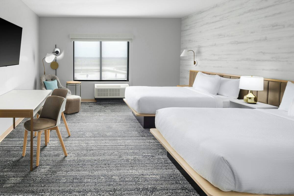 Habitación de hotel con dos camas, un escritorio, una silla, una mesita y ventana con vistas.